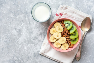 oatmeal with banana, almonds nuts and kiwi slices in pink bowl, glass of milk, napkin on gray concrete background Top view Healthy breakfast or lunch Natural ingredients Rustic style