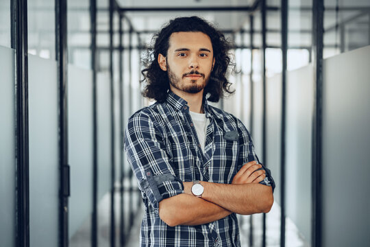 Portrait of young curly casually dressed male entrepreneur standing in a glass corridor