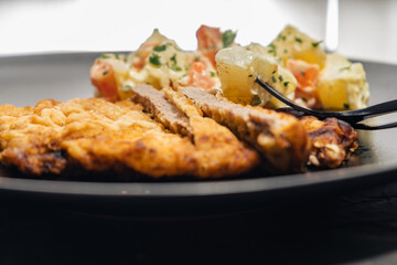 Black plate with a meat schnitzel and Russian salad of potatoes, carrots, peas, egg and mayonnaise, all homemade and natural. Food concept.