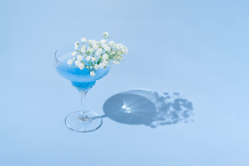 Minimal summer cocktail drink with white flowers on a bright pastel blue background. Sunlight glass...
