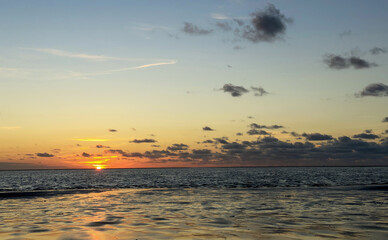 View of the setting sun shining on the Sea and reflected on the beach, clouds with sun-shining...