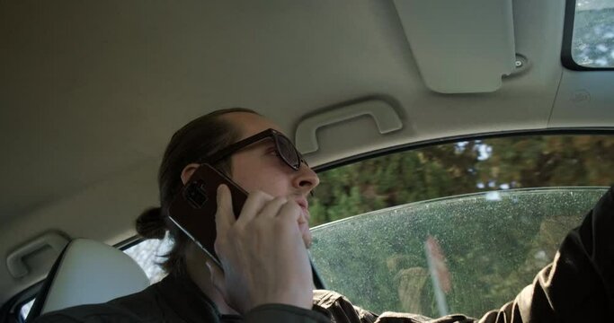 Low angle of young man talking on the phone while driving. 