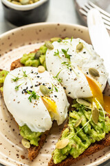 Healthy sandwich with avocado and poached eggs. Delicious breakfast or snack on a light background, top view