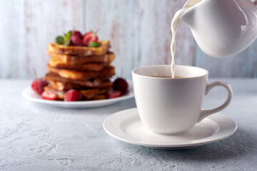 A cup of coffee with cream and French toast with cinnamon and strawberries. Morning breakfast