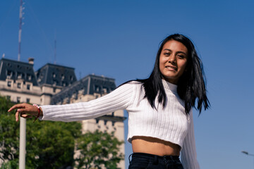 Medium shot of a black haired Latin woman dancing with some old building and blue sky in the background. Space for writing.