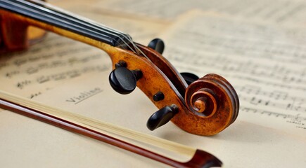 An old antique violin and a bow on a table with yellowed sheet music close-up. © Irina