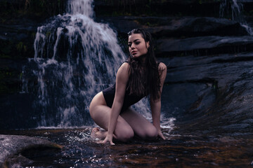 young woamn model posing for fashion photoshoot in a waterfall with long black hair and black swimsuit