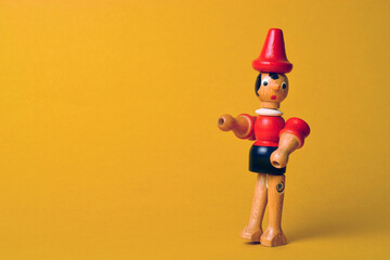 Wooden puppet depicting Pinocchio walking on a yellow background