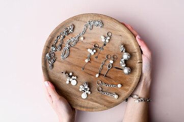 Top view of women's hands hold a wooden plate with stylish jewelry set on pink background. Fashion concept