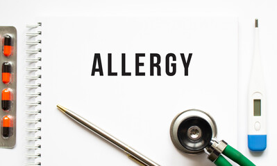 ALLERGY text written in a notebook lying on a desk and a stethoscope.