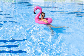 Summer sale. Young sexy woman in bikini swimsuit, sunglasses with pink flamingo relaxing in blue pool water. Summer luxury vacation in spa resort pool.