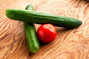 two cucumbers and a tomato on a wooden surface