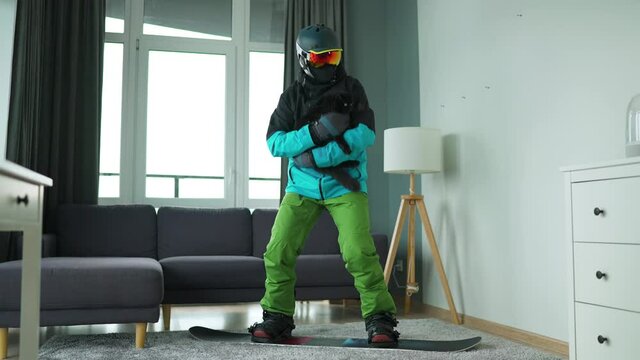 Fun video. Man dressed as a snowboarder depicts snowboarding on a carpet in a cozy room with fluffy cat. Waiting for the start of the winter