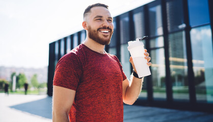 Happy athletic man with bottle of water on street