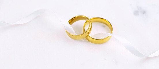 Banner with two golden wedding rings close up with ribbon on white background. Wedding invitation...