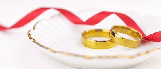 Banner with two golden wedding rings close up with ribbon on white background. Wedding invitation card concept. 