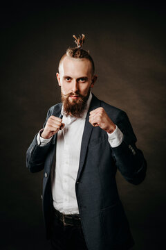 Portrait of a young bearded brutal hipster man, in a fighting stance in a jacket and white shirt in the studio on a dark background