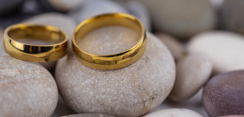 Banner with two golden wedding rings close up on gray pebble stones. Wedding on the beach invitation card concept.