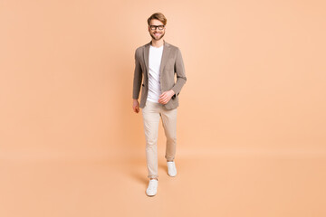 Fototapeta na wymiar Full body photo of cheerful charismatic young man walk good mood smile isolated on pastel beige color background