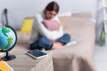 smartphone with blank screen on table near blurred teenage girl