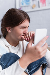 sad teenage girl covering mouth while crying and holding smartphone