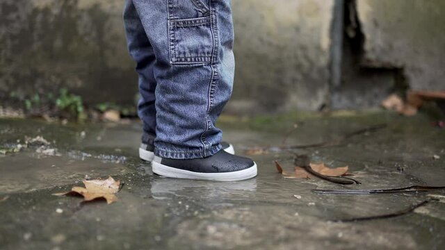 Child jumping into water puddle. Toddler wearing boots splash into puddle