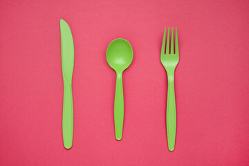 Green plastic forks, spoons, knifes on pink paper. Set of plastic cutlery in different spoons forks...