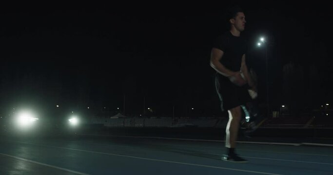 Cinematic shot of young disable man with legs prosthesis running with effort with racing auto behind on car track at night. Concept of handicapped people active lifestyle, determination, motivation.