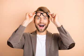 Photo of attractive excited young guy wear jacket arms spectacles big eyes open mouth isolated beige color background