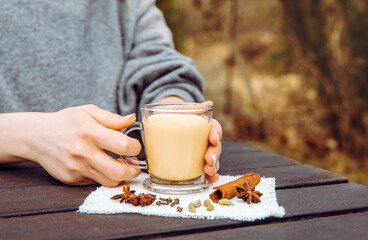 Close up view of woman hands holding cup of Chai latte with cinnamon outdoors in spring. Picnic...