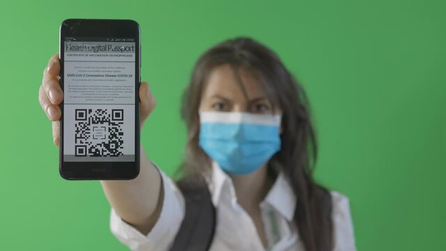 Young woman with face mask shows smartphone for scanning the digital health certificate passport, front view isolated on green screen chroma key
