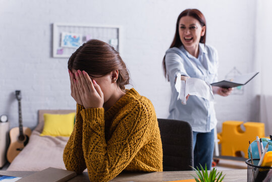 Teenage Girl Covering Face With Hands Near Angry Mother Tearing Papers In Notebook