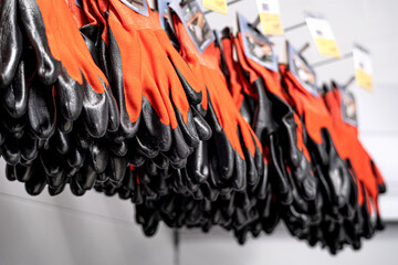 Orange rubberized gloves hang in the store on a light background. Safety precautions, hand protection during operation. Light background.