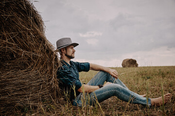 Naklejka na ściany i meble A man in a hat next to a haystack