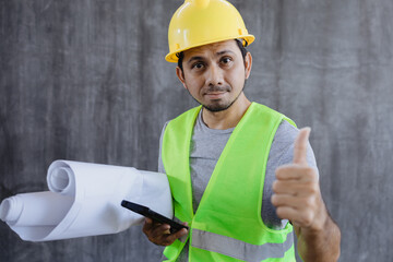 Fototapeta premium Asian construction worker hold blueprint and smartphone with making thumb up sign like