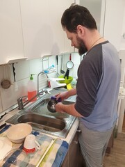 a bearded tired and nervous man washes dishes in the kitchen sink after dinner