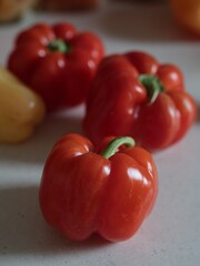 Vertical close up still life of three red ripe bell peppers on a white kitchen surface.