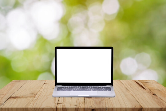 Laptop on wood table with green bokeh nature background