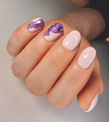 Trendy pink gel nail polish with an abstract purple fluid design. Manicure of soft pink color with a beautiful spreading pattern. Pastel color coating on the nails with purple design and silver.