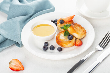 Cottage cheese pancakes, syrniki, with honey and berries in a white plate, horizontal view, restaurant serving, breakfast