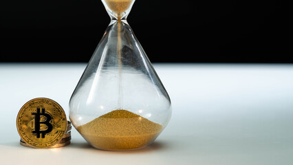 Gold Bitcoin and hourglass on white table with black background. Macro shot. Time is money,...