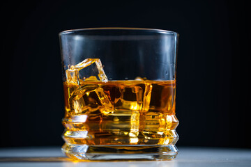 Whiskey poured into a glass with ice, in slow motion, macro shooting, on a wooden table and dark background. Concept: alcohol, spirits, for a good evening, alcohol harms health