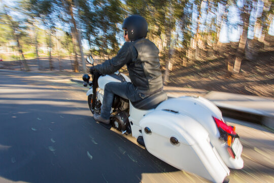 Motorcyclist dressed in leathers riding down a canyon street with trees blurred