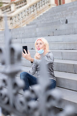 girl lowers her surgical mask and sticks out her tongue to the mobile