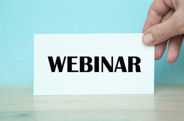 THE WORLD WEBINAR written on the notebook. Notebook in hand on a blue background.Business concept for online education event written on notepad paper.