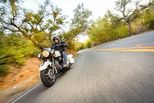 Motorcyclist dressed in leathers riding down a canyon street with trees blurred