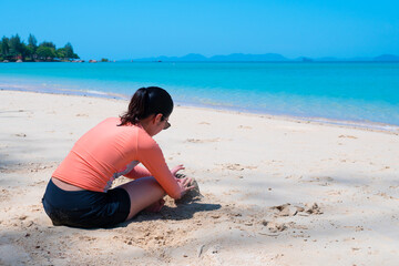 young asian woman building sandcastle at the beautiful beach of island on summer vacation. travel concept