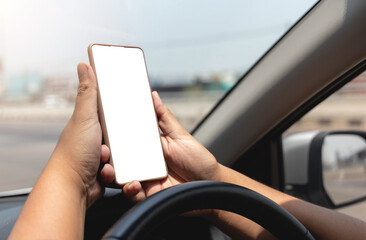 Close-up of hand holding smartphone with white mockup on screen, background of car steering wheel.