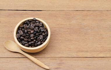 roasted coffee beans in a wooden bowl on a rustic wooden table with a spoon. Selective focus on coffee beans in a bowl