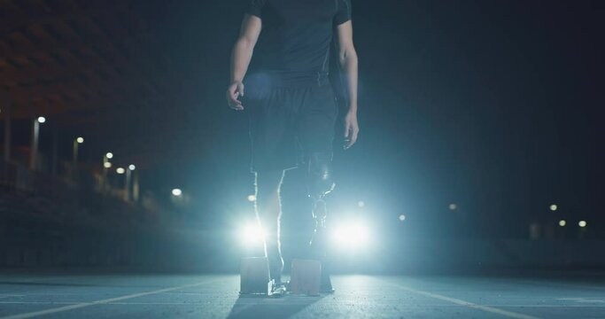 Cinematic shot of young disable man with legs prosthesis launching off the start line with racing auto behind on race track at night. Concept of handicapped people active lifestyle, determination.